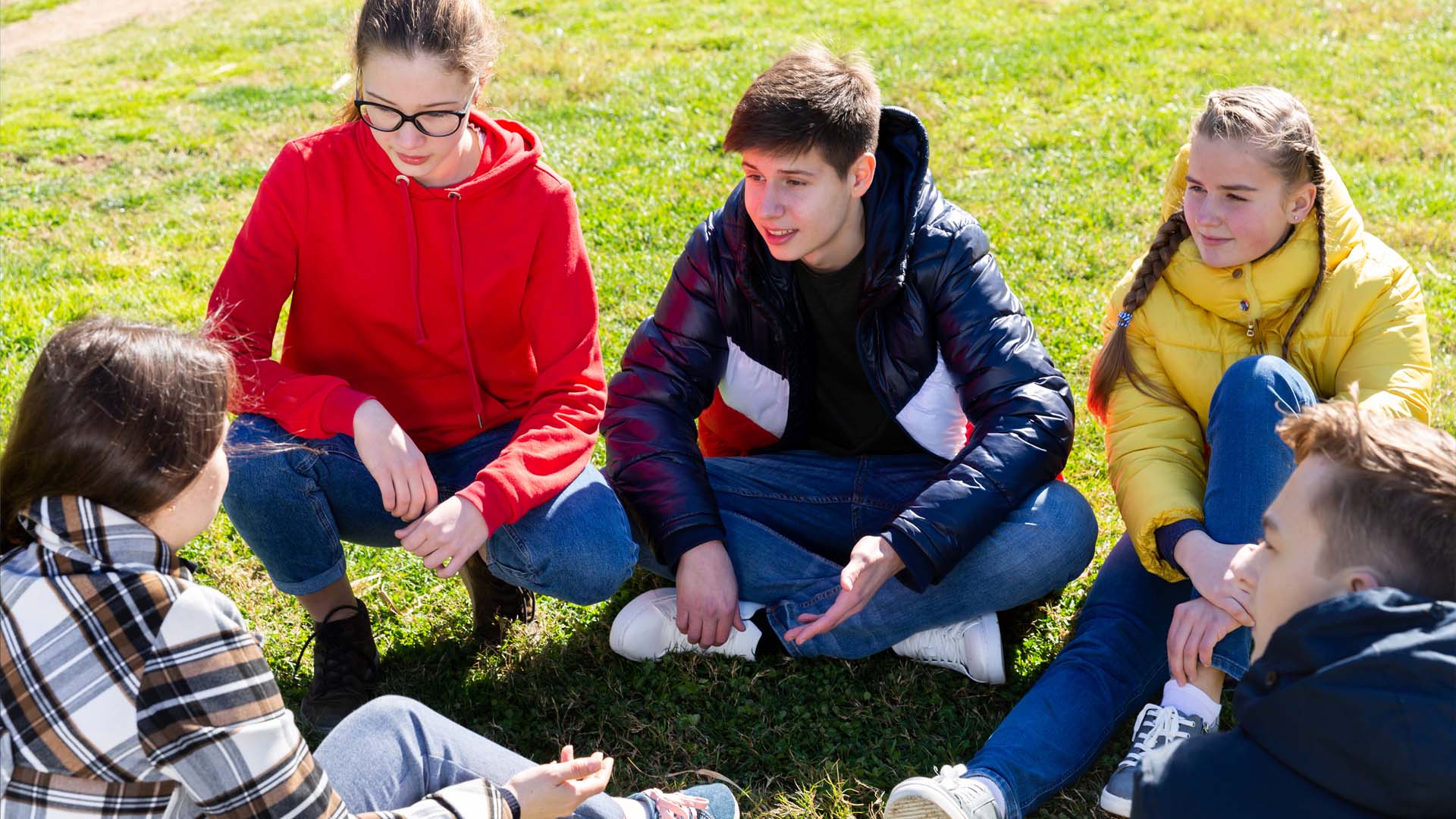 En gruppe teenagere sidder sammen på græsset og taler. FOTO: AdobeStock